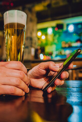 man hand hold smartphone, drinking beer and reading message at bar or pub