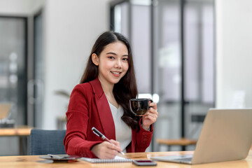 Beautiful young Asian businesswoman holding a coffee mug working at office. Looking at camera.