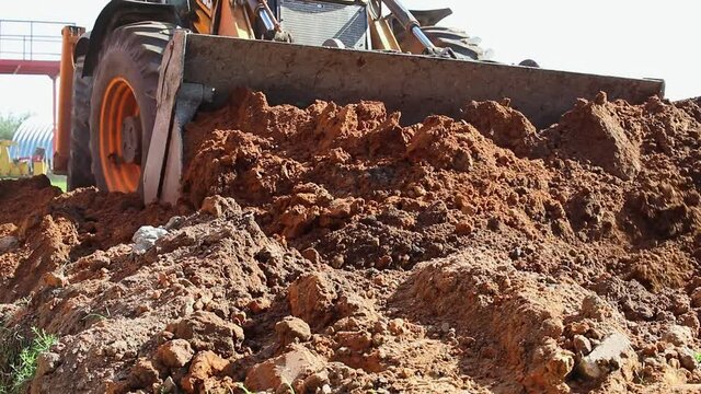 The excavator backfills the pit with the front bucket. Moves soil around the construction site. Close-up. Heavy construction equipment.