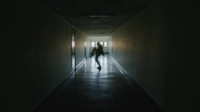 Silhouette of young tender woman, dancing contemporary dance in long dark hallway, in counter light, practicing alone, working hard to gain new skills, Zoom in, Slow motion.