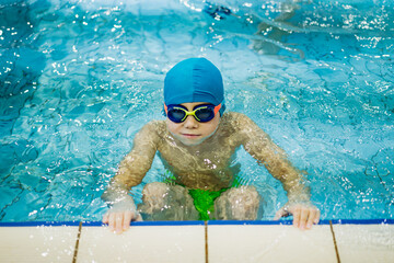 little caucasian boy wearing goggles going. to start swimming the backstroke in a pool