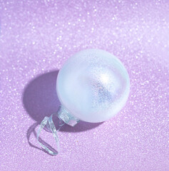 White mother-of-pearl Christmas ball on a lilac shiny background. Card