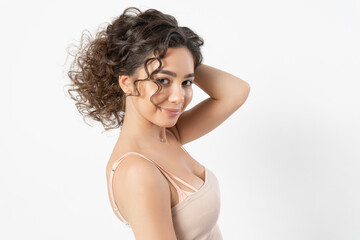 A beautiful young female model with curly long dark hair curled on a curling iron smiles and poses for a portrait on a white background.