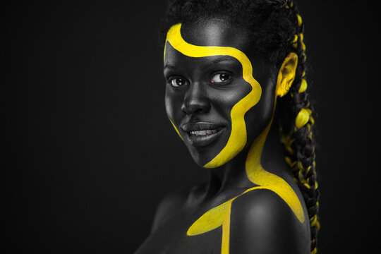Yellow and black body paint. Woman with face art. Young girl with colorful bodypaint. An amazing afro american model with makeup.