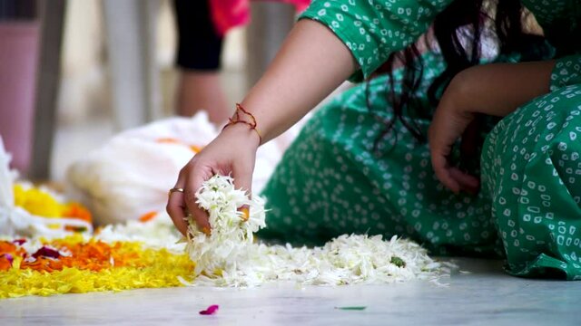 slow motion shot of Indian woman dropping marigold jasmine flowers on a rangoli pattern on the floor while making a rangoli for diwali, new year or a wedding decoration as part of the hindu religion