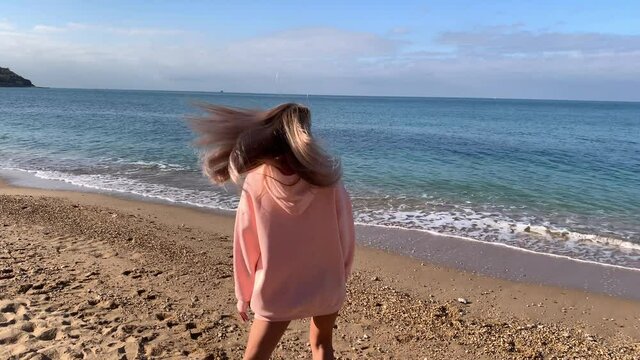 A beautiful blonde woman, in a warm jacket and boots, rushed to rest in the fall. Looks at the sea, rejoices, jumps, circles and smiles.