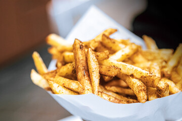 Crispy spicy french fries packed with white paper. Tasty vegan food fried potatoes.