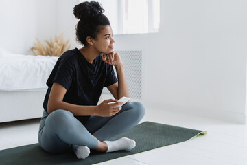 Thoughtful african ethnicity woman with smartphone resting after sport training