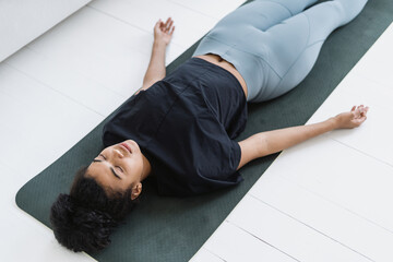 Afro american female lying on sport mat, resting after training