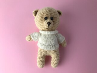 soft knitted bear on a pink matte background. bear for a gift, a toy for children. knitted bear, beige. bear is made of natural material