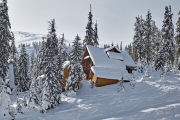Fantastic winter landscape with wooden houses in snowy mountains. Hight mountain peaks in foggy sky. Christmas and winter vacations holiday concept
