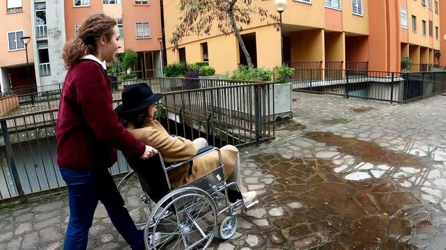 assistance to a disabled person - woman pushes the wheelchair of a young man