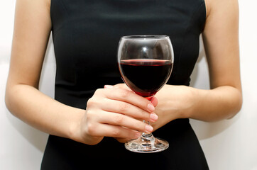 A woman holds a glass goblet with red wine in her hands, to celebrate the holiday. Close-up, soft focus.