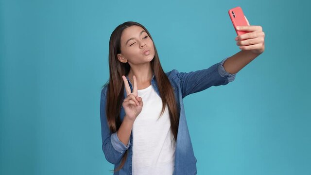 Brown hair kid make selfie device post v-sign isolated blue color background 