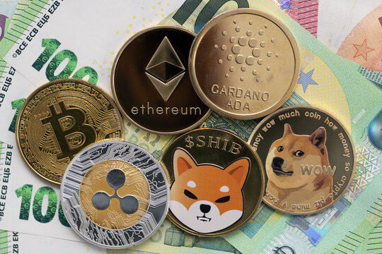 Bitcoin, Cardano, Shiba Inu, Ethereum, Ripple, and Dogecoin physical coins laying on top of 100 and 10 Euro bills.