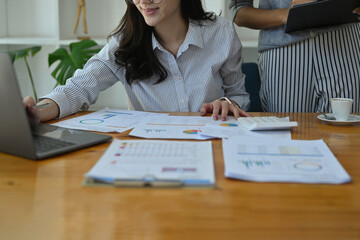 Photo of office women sitting and standing while working together at the wooden working desk...