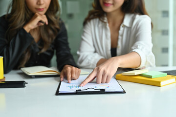 Fototapeta premium Photo of two female designers working together at the white working desk surrounded by clipboard, notebook and office equipment.