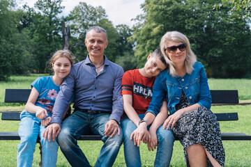 Photo portrait of a family sitting on a bench in a park.