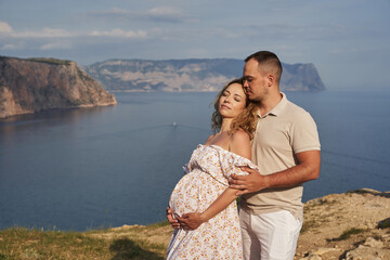 beautiful young couple on the background of the sea. the woman is pregnant. love, tenderness, family