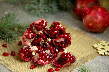 selective focus on red juicy pomegranate against the background of green branches of a Christmas tree and blurry spots of a garland, decoration of a festive table, festive cooking treats