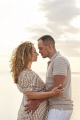 beautiful young couple stands on a rocky sea shore in the sunset rays face to face, trying to kiss. they hug, the woman is pregnant. warmth and love, happiness