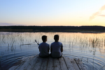 Kids sitting on wooden bridge by lake at sunset