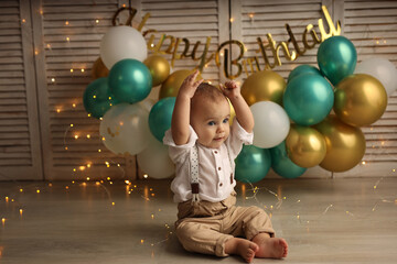 Cute blond kid in a festive shirt and trousers. A happy kid on the background of balloons with...
