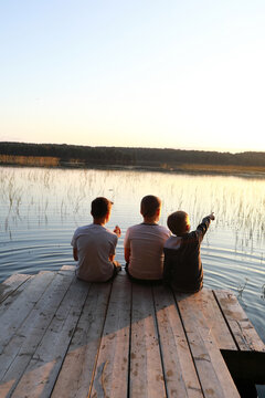 Boys resting on wooden bridge by lake at sunset