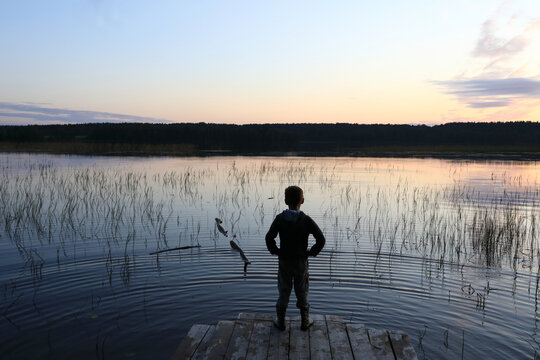 Child standing on wooden bridge by lake at sunset