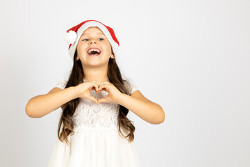 portrait of laughing, cheerful girl with long curls in white dress, wearing red Santa Claus hat...