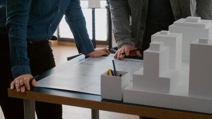 Close up of colleagues working on urban design with blueprints and building model. Team of people...