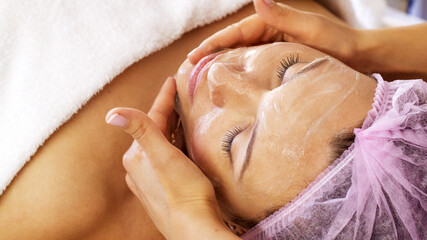 Woman in a spa salon on cosmetic procedures for facial care. Cosmetologist applies  a cosmetic...