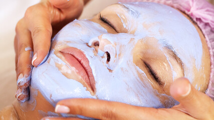 Beautician makes a massage of the face with a moisturizing cream. Cosmetologist doing a woman a...