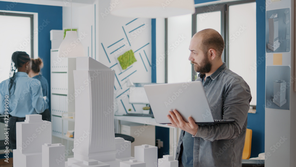 Aufkleber man holding laptop to work on building model design and blueprints plan. architect using computer an