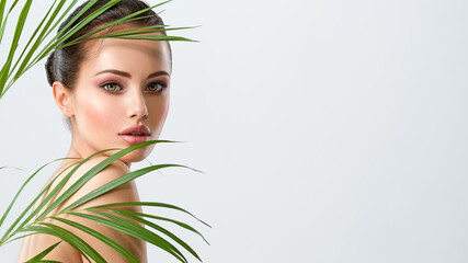 Young beautiful woman with healthy skin of face and palm leaves. Closeup fresh face of an...