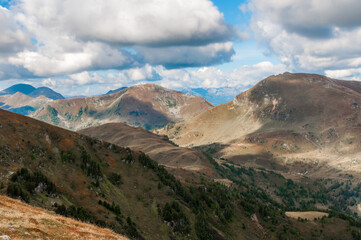 Fototapeta na wymiar Bergige Landschaft in Österreich. Blick von einem hochgelegenen Punkt auf eine Gebirgskette. Sonniger Herbsttag mit dramatischen Wolken