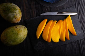 Ripe and tasty egyption Mango sleces and whole mango served at black dish. flat lay