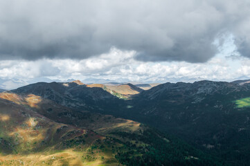 Obraz na płótnie Canvas Bergige Landschaft in Österreich. Blick von einem hochgelegenen Punkt auf eine Gebirgskette. Sonniger Herbsttag mit dramatischen Wolken