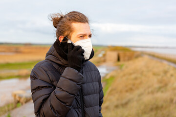 A young man wearing a KN95 one use facemask while using his mobile phone during the Covid-19 corona...