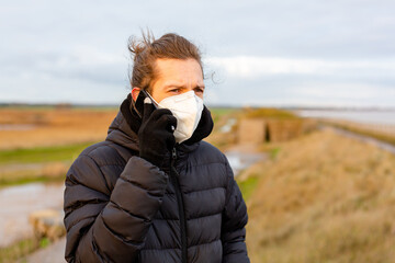 Fototapeta premium A young man wearing a KN95 one use facemask while using his mobile phone during the Covid-19 corona virus pandemic