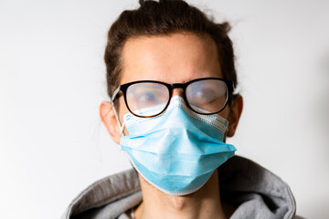Young man with foggy glasses caused by wearing disposable mask. Protective measure during coronavirus pandemic