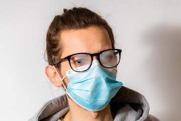 Young man with foggy glasses caused by wearing disposable mask. Protective measure during...