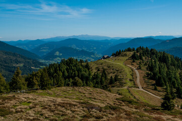 Fototapeta na wymiar Bergige Landschaft in Österreich . Blick über eine Weide auf einen Weg, der zu einer Jausenstation führt. Sonniger Herbsttag