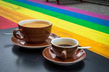 Two cups of coffee on a table in a rainbow street. Equal rights for LGBTQ+ community concept. Skólavörðustígur, Reykjavik - Iceland. - obrazy, fototapety, plakaty