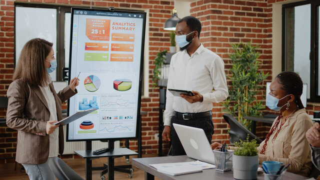 Diverse coworkers meeting to plan business growth and project during coronavirus pandemic. People working together to design marketing strategy and data analysis for financial presentation. - Powered by Adobe