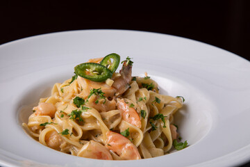 Italian pasta with prawns chili pepper and greens. Italian food, white dish, dark background