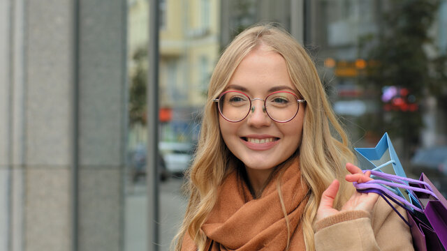 Portrait caucasian happy woman female shopper smiling holding in hand bright gift bags young lady in glasses standing on street after shopping girl enjoying discounts and sales in city center store