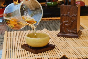 Fragment of traditional serve tea on tea ceremony. Misted transparent with condensate drops glass teapot with green tea and special semi-gloss light-green glazed ceramic crackle tea bowl on foreground