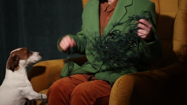 woman in a stylish woolen jacket sits in an armchair and tries to untangle the Christmas garlands