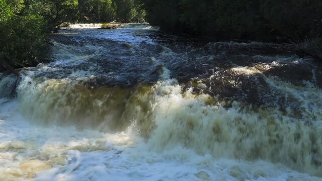 The Lower Falls of Tahquamenon Falls; rapid, rushing water over rocks spilling into foam--front view, medium close